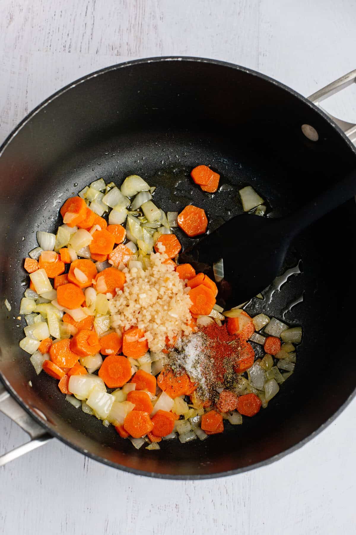 Stirring garlic and spices in a pot with softened onions and carrots.