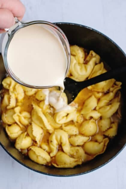 Pouring milk into a pot of cooked tortellini.