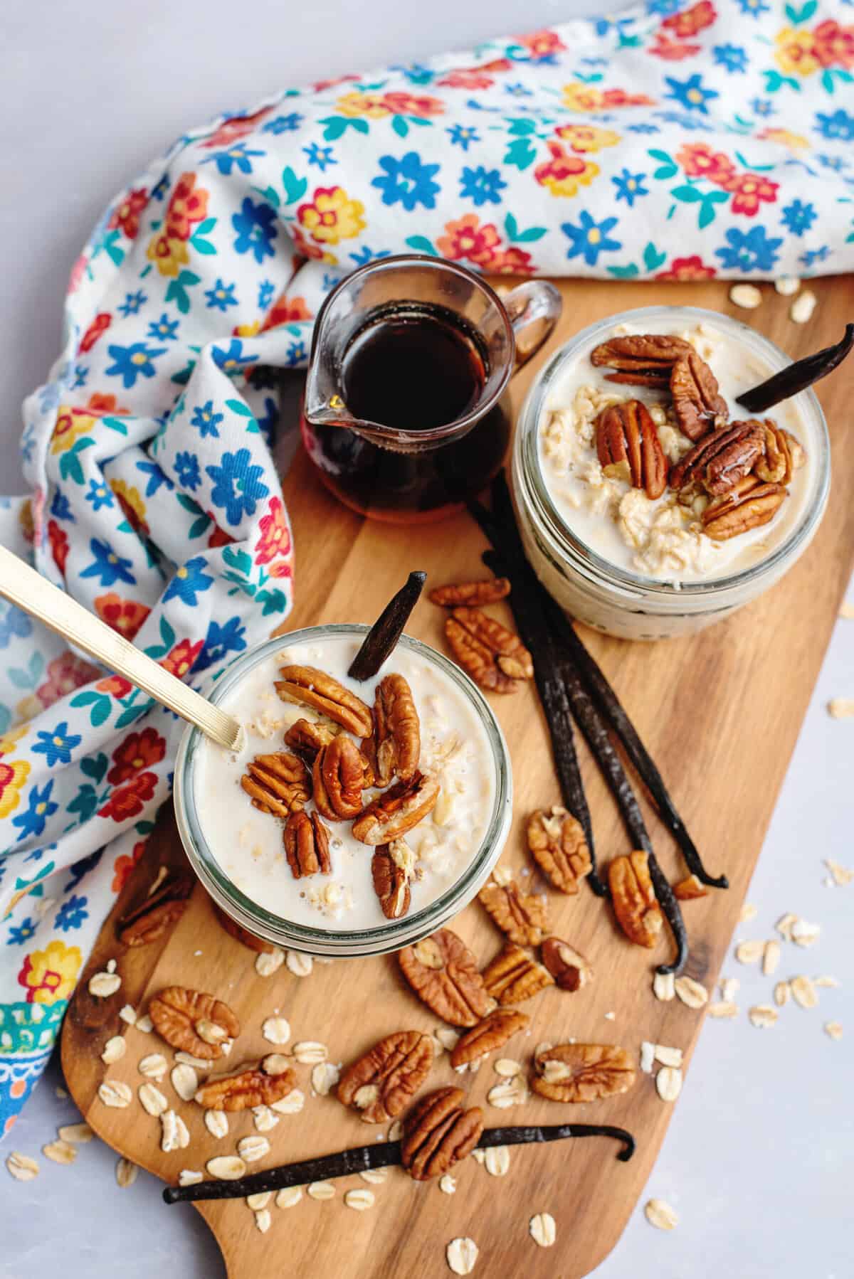 Jars of vanilla maple overnight oats topped with pecans on a wooden cutting board.