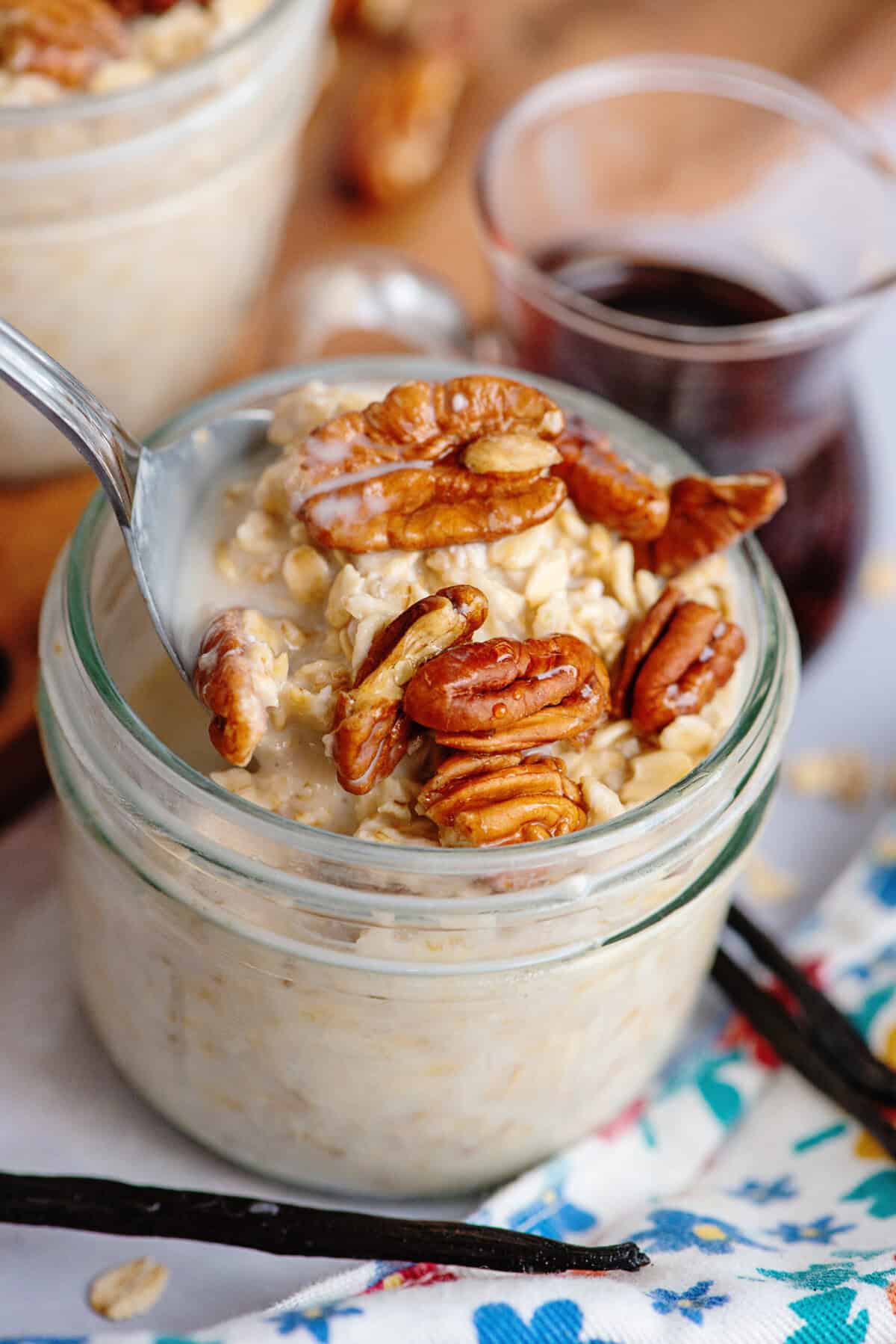 A spoon lifting overnight oats with pecans out of a mason jar.