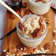Vanilla maple overnight oats in mason jars topped with pecans over a wooden cutting board.