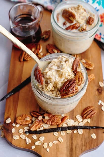 Vanilla maple overnight oats in mason jars topped with pecans over a wooden cutting board.