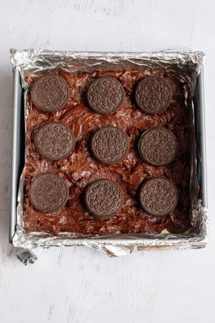 Rows of Oreo cookies layered on brownie batter in a baking pan.