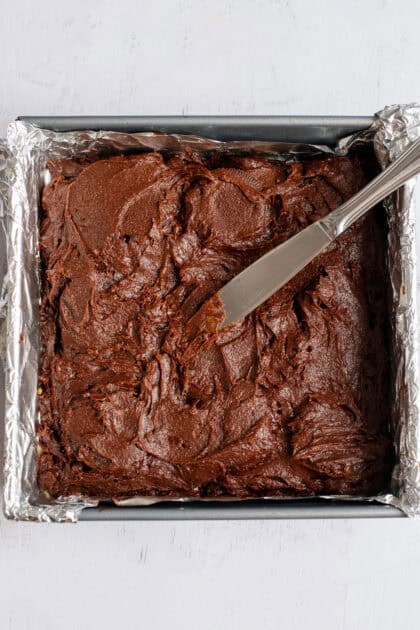Spreading brownie batter with a knife over Oreo cookies.