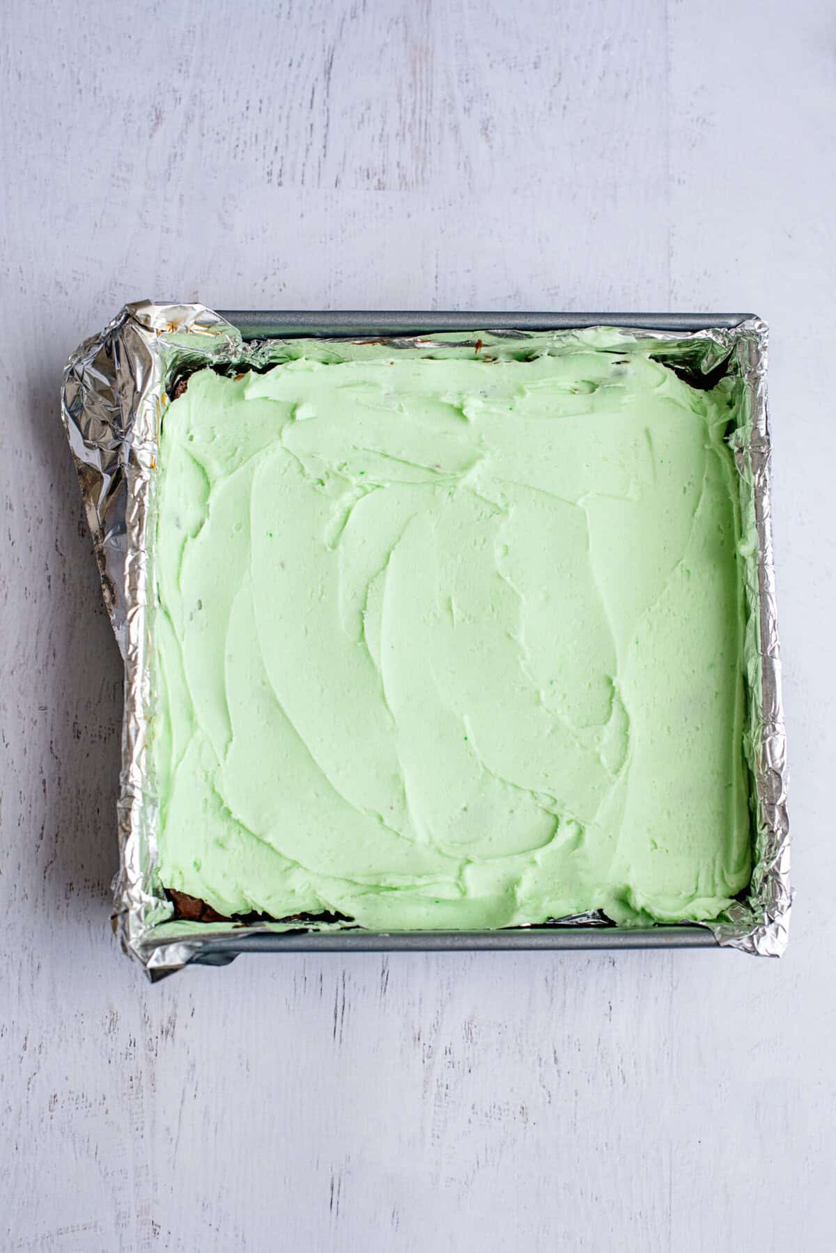 Green filling over brownies in a tin foil lined baking pan.