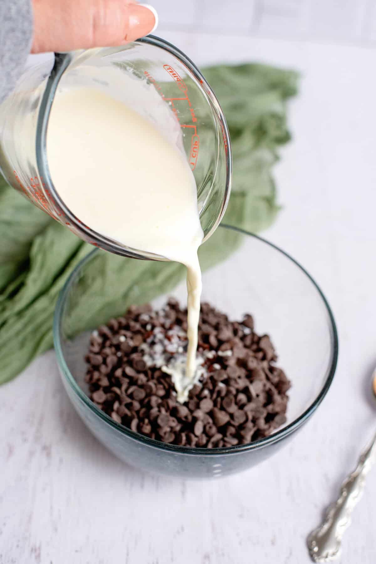 Pouring heavy cream into a glass bowl of chocolate chips.