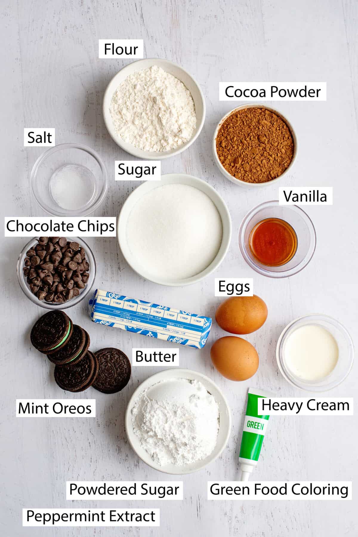 Ingredients for grasshopper brownies, including butter, sugar, eggs, cocoa powder, all-purpose flour, semi-sweet chocolate chips, mint chocolate sandwich cookies, powdered sugar, heavy cream, peppermint extract, green food coloring, and chocolate chips.