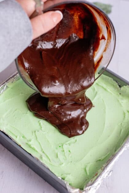 Pouring chocolate ganache over minty green brownies.