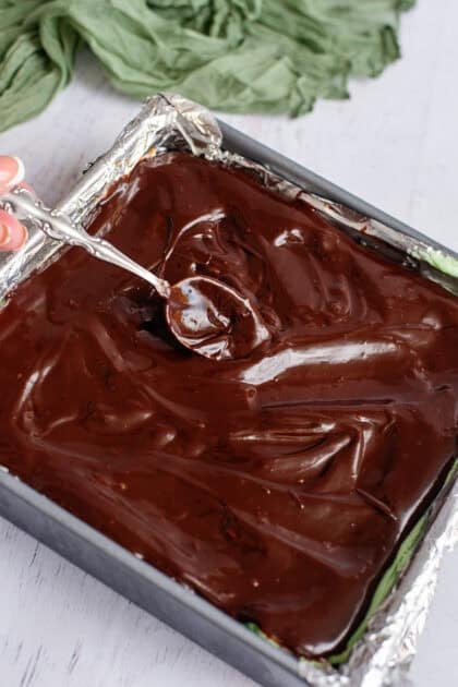 Spreading chocolate ganache over brownies with a spoon.