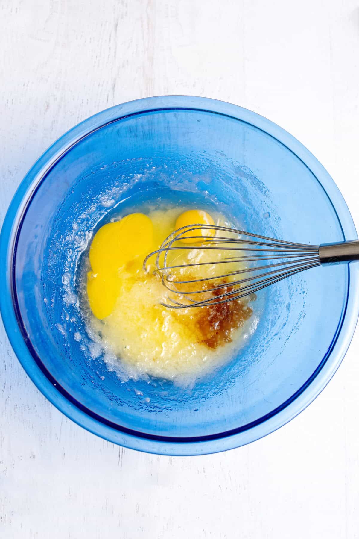 Whisking eggs and vanilla in a glass blue mixing bowl.