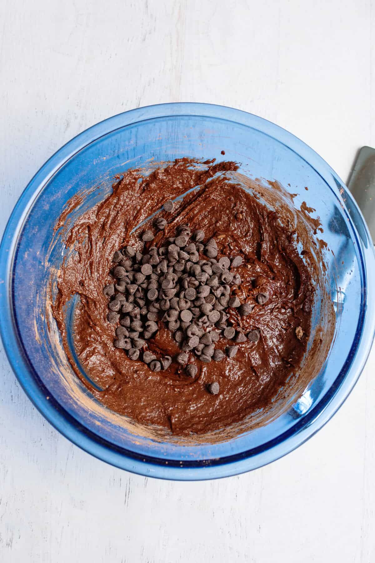 Chocolate chips in a glass blue mixing bowl over brownie batter.