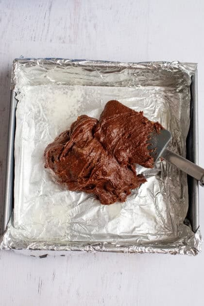 Spreading brownie batter on a baking pan lined with tin foil.
