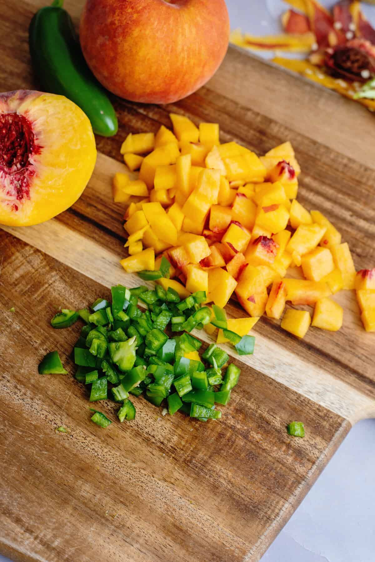 Diced peaches and minced jalapenos on a wooden cutting board.