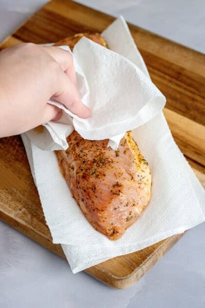 Patting a pork tenderloin with paper towel on a cutting board.