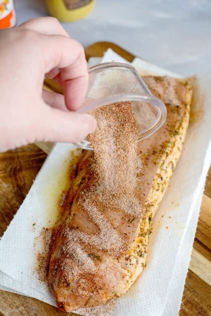 Pouring seasoning onto a pork tenderloin.