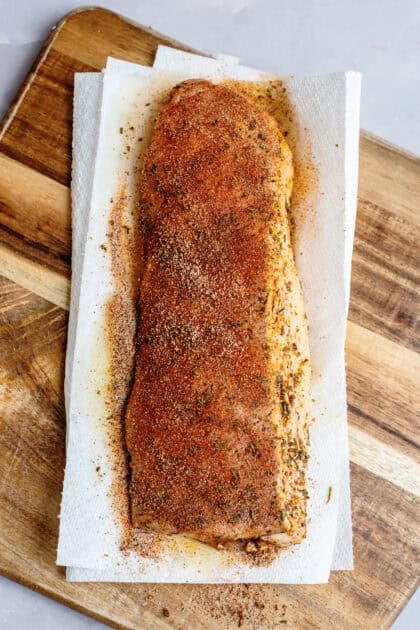 Pork tenderloin rubbed with seasoning on a wooden cutting board.