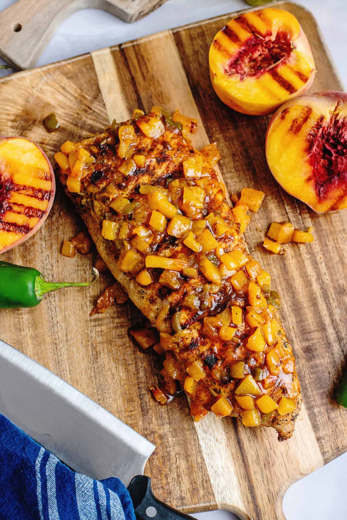 Grilled peach jalapeno glazed pork tenderloin resting on a wooden cutting board.