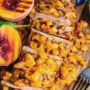 Grilled peach jalapeno glazed pork tenderloin sliced on a cutting board surrounded by fresh peaches and jalapenos.