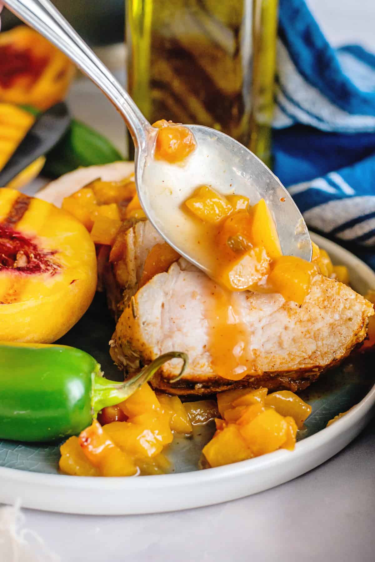 A spoon with glaze dripping from it onto gilled peach jalapeno glazed pork tenderloin on a plate.