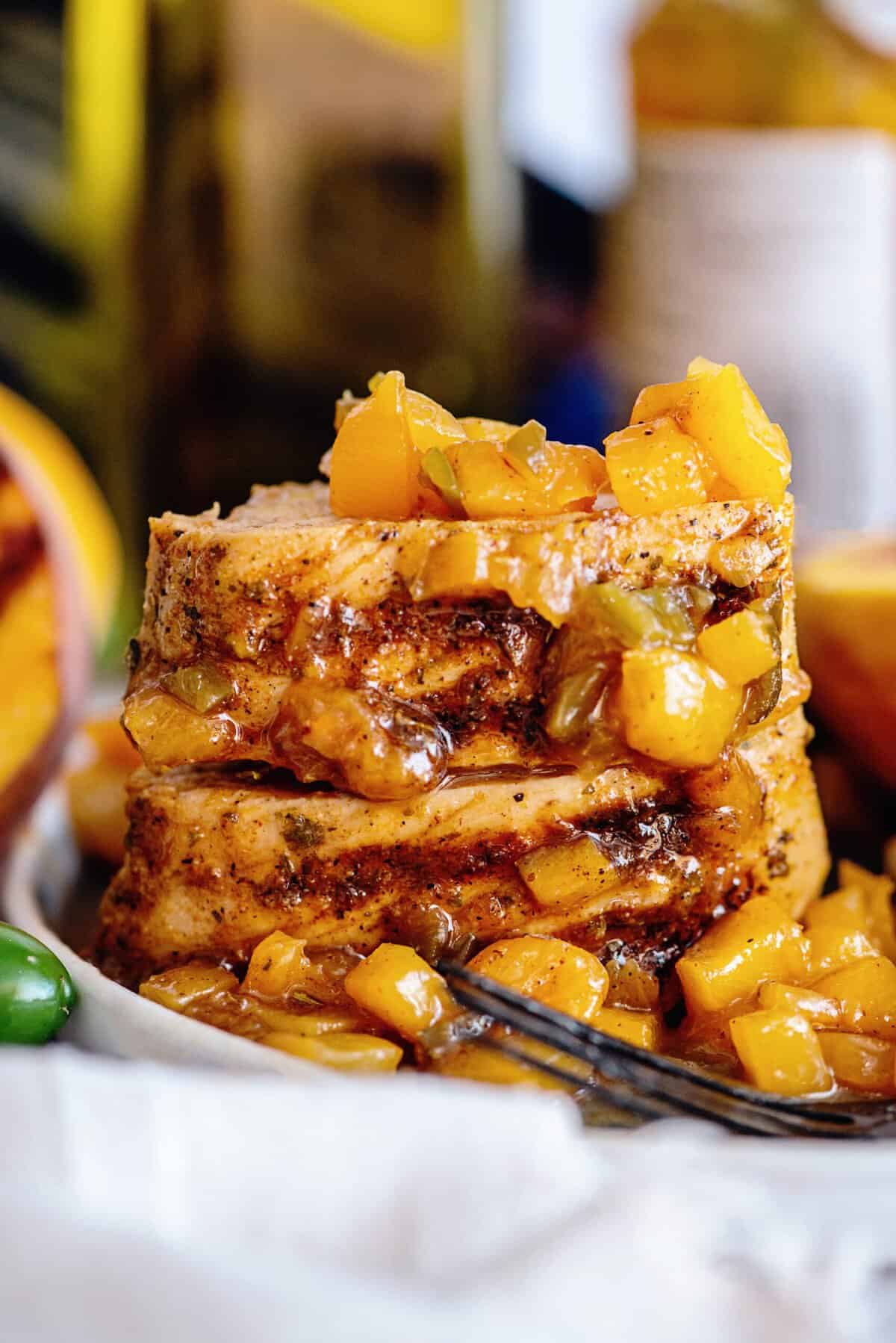 Grilled peach jalapeno glazed pork tenderloin slices stacked on each other on a plate.