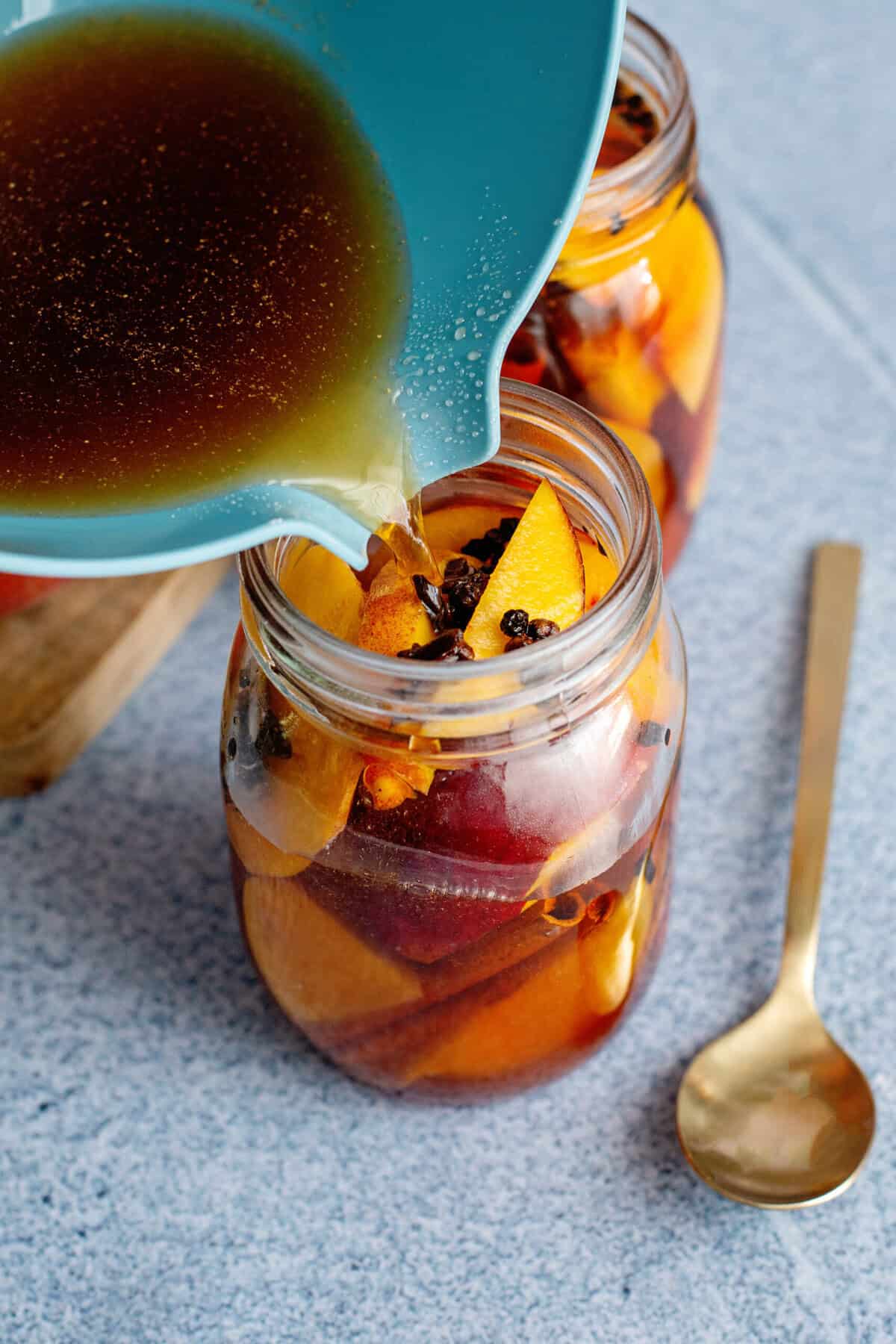 Pouring hot brine over slices peaches in a mason jar.