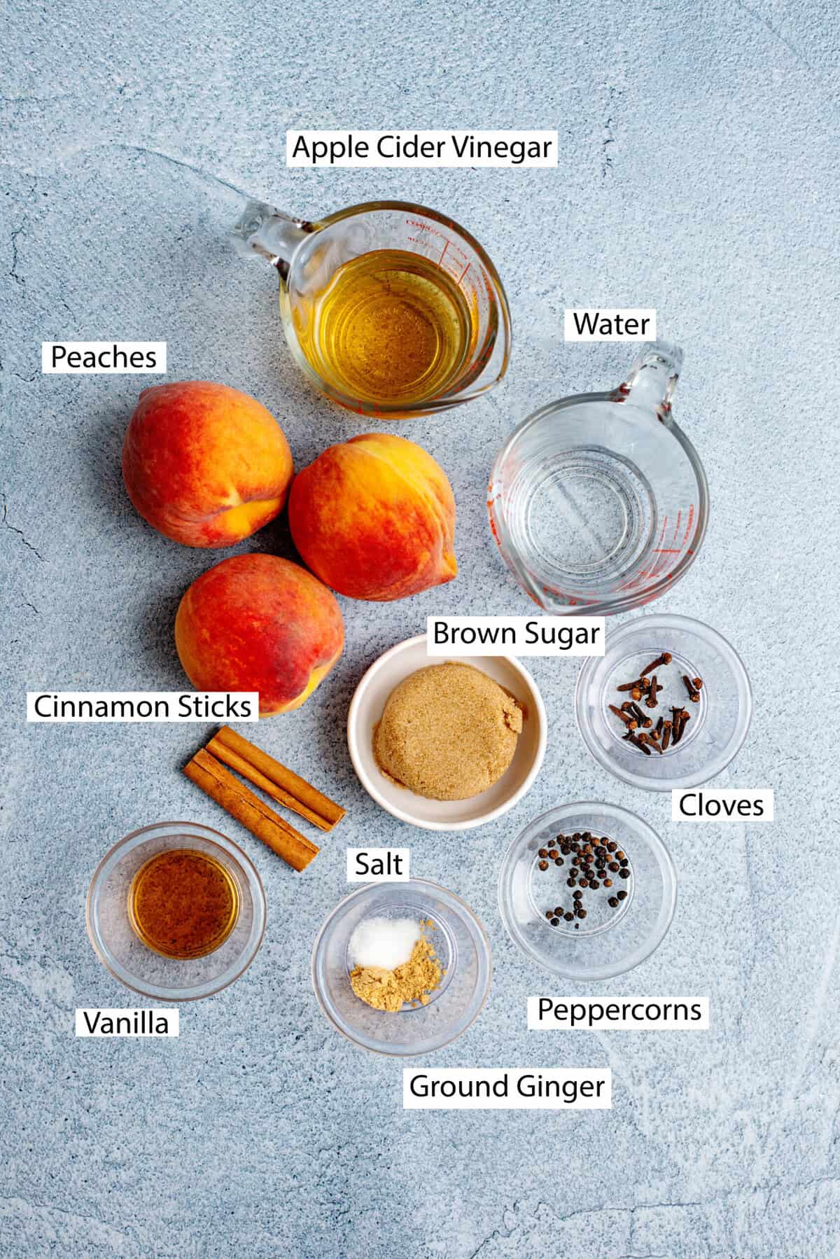 Ingredients for pickled peaches, including peaches, apple cider vinegar, light brown sugar, cinnamon sticks, whole cloves, whole black peppercorns, ground ginger, kosher salt, and vanilla extract.