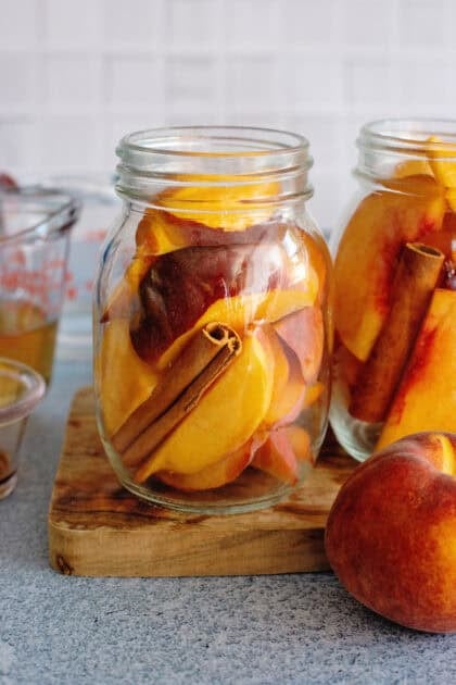 Sliced peaches in mason jars with cinnamon sticks.