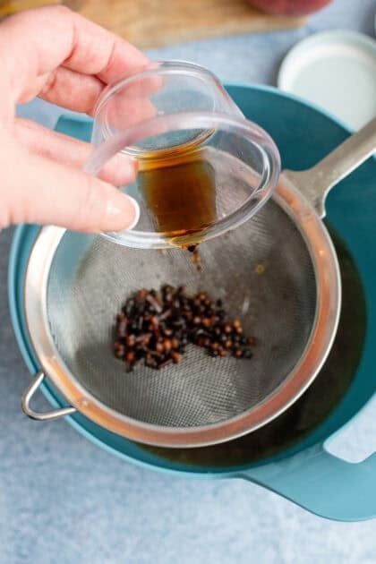 Pouring vanilla through a strainer with whole cloves and peppercorns.