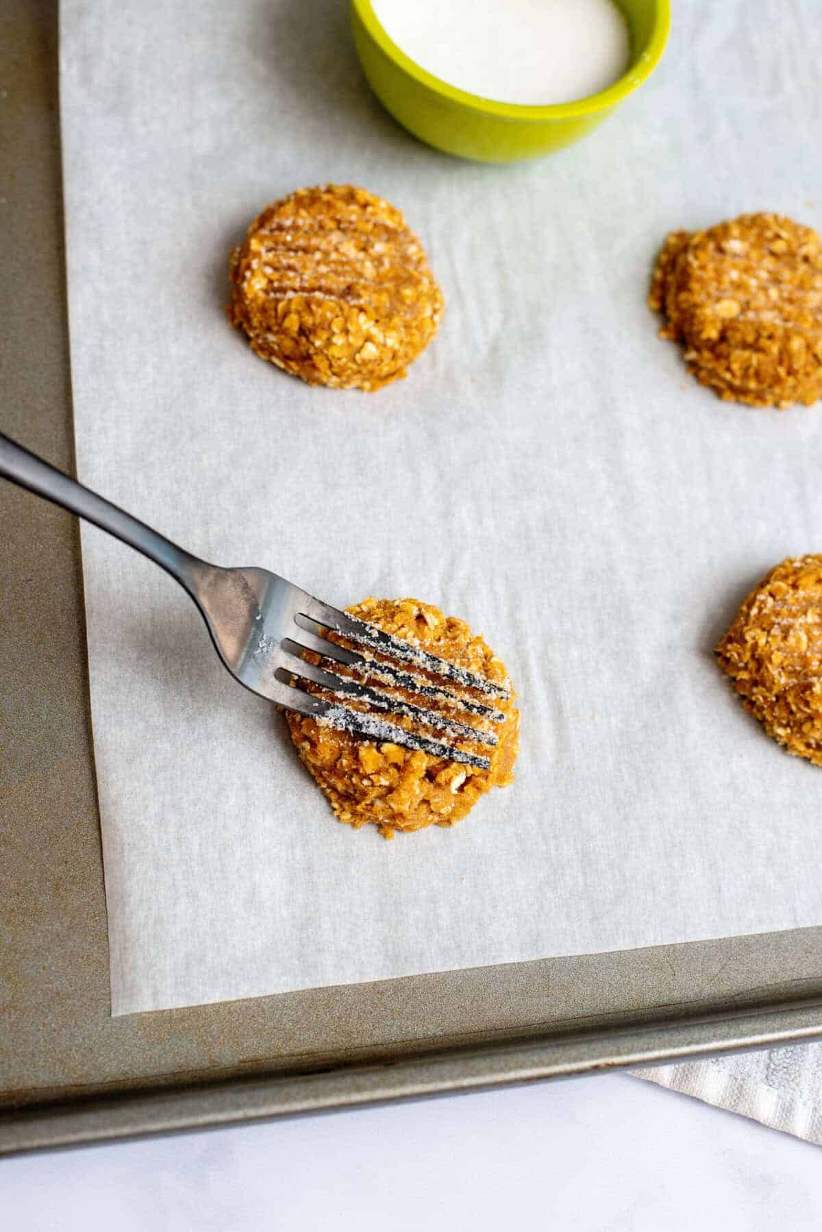 Sugar-dipped fork pressing onto pumpkin oatmeal cookie dough balls on a baking sheet.