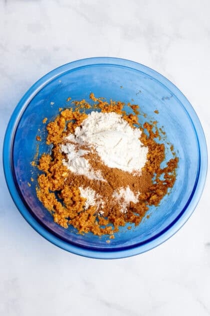 Adding flour to cookie dough in glass blue mixing bowl.