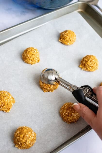 Adding scoops of pumpkin oatmeal cookie dough onto a baking sheet.