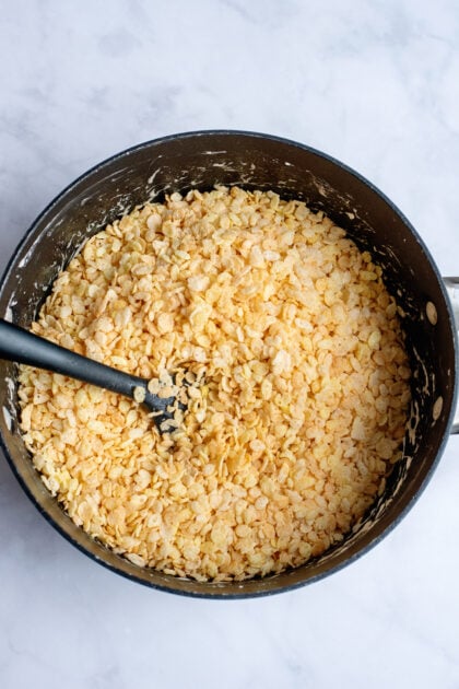 Mixing Rice Krispie cereal into a pot with melted marshmallows.
