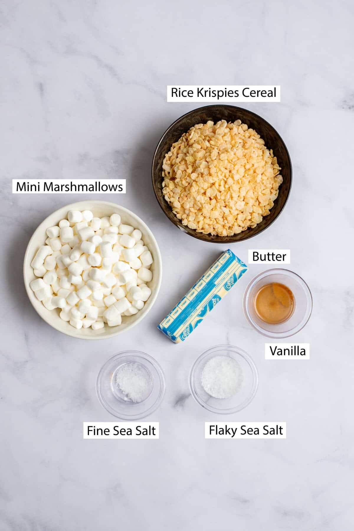 Ingredients for brown butter sea salt rice krispies, featuring unsalted butter, mini marshmallows, vanilla extract, fine sea salt, Rice Krispies cereal, and flaky sea salt.