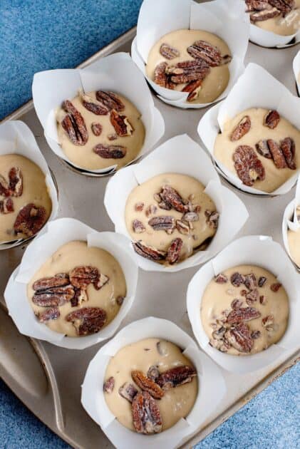 Muffin liners filled with batter and topped with pecans