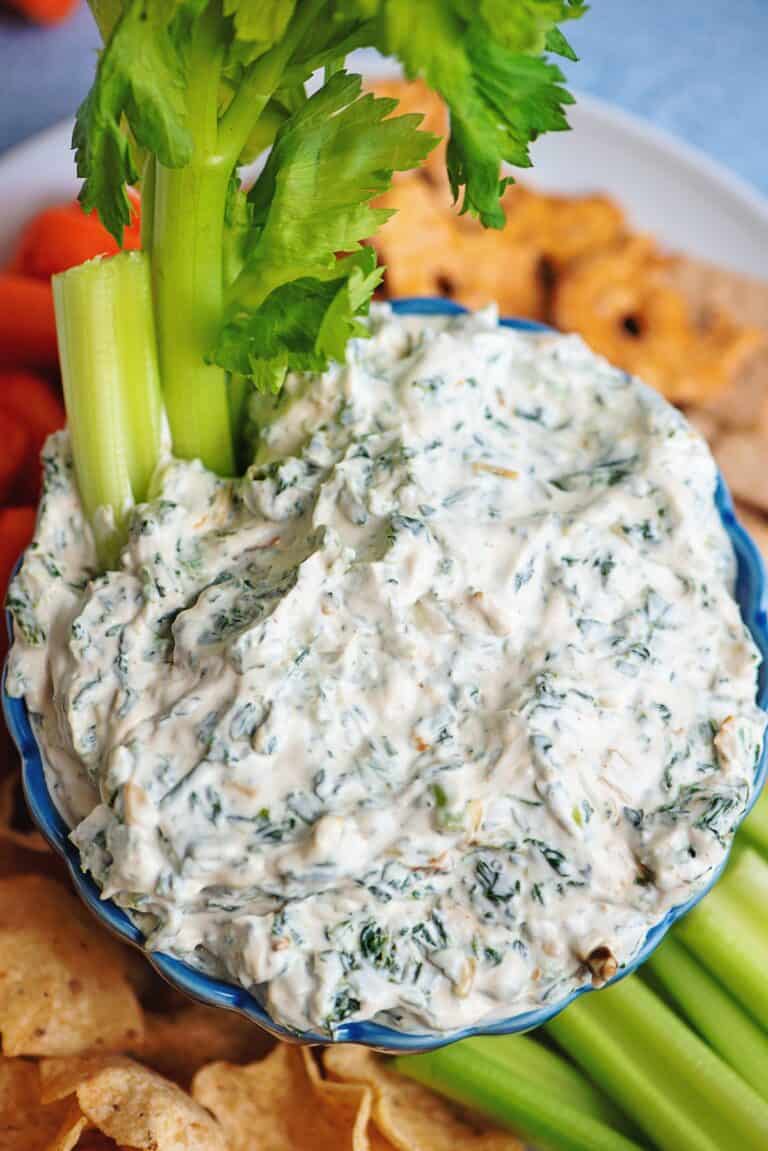 Creamy spinach dip in a blue bowl with celery and crackers